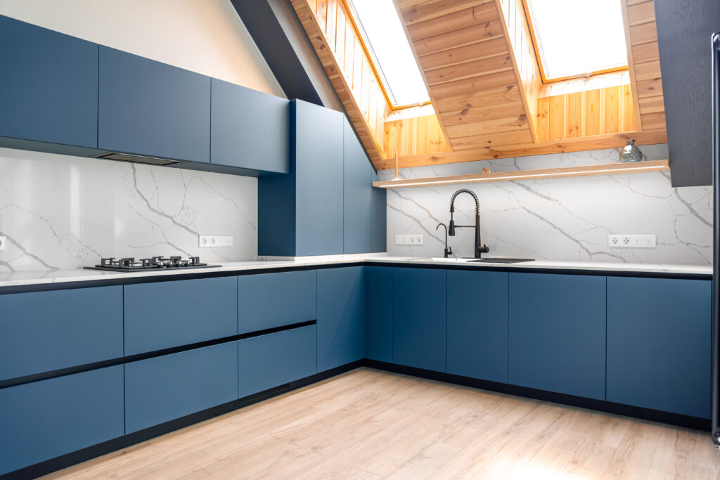 Spacious L shaped kitchen under skylights with matte blue handleless fronts, a white marble backsplash and quartz countertop. Daylight and LED accents create a soft Scandi vibe.
