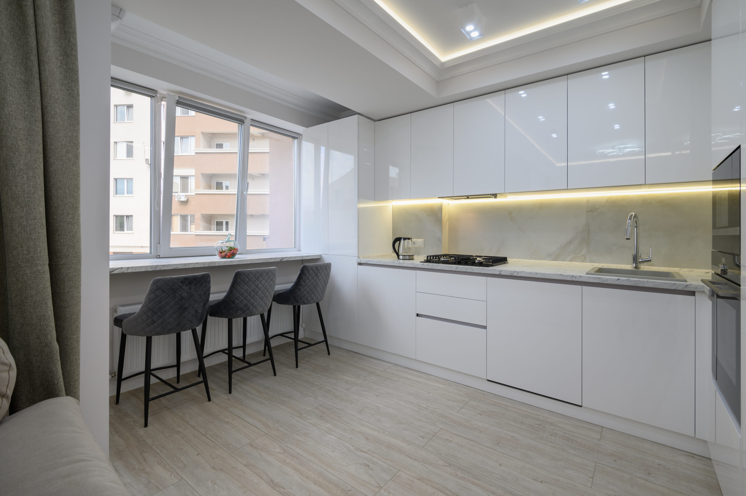 Kitchen with a stove top, dining chairs next to a window, city view outside of window