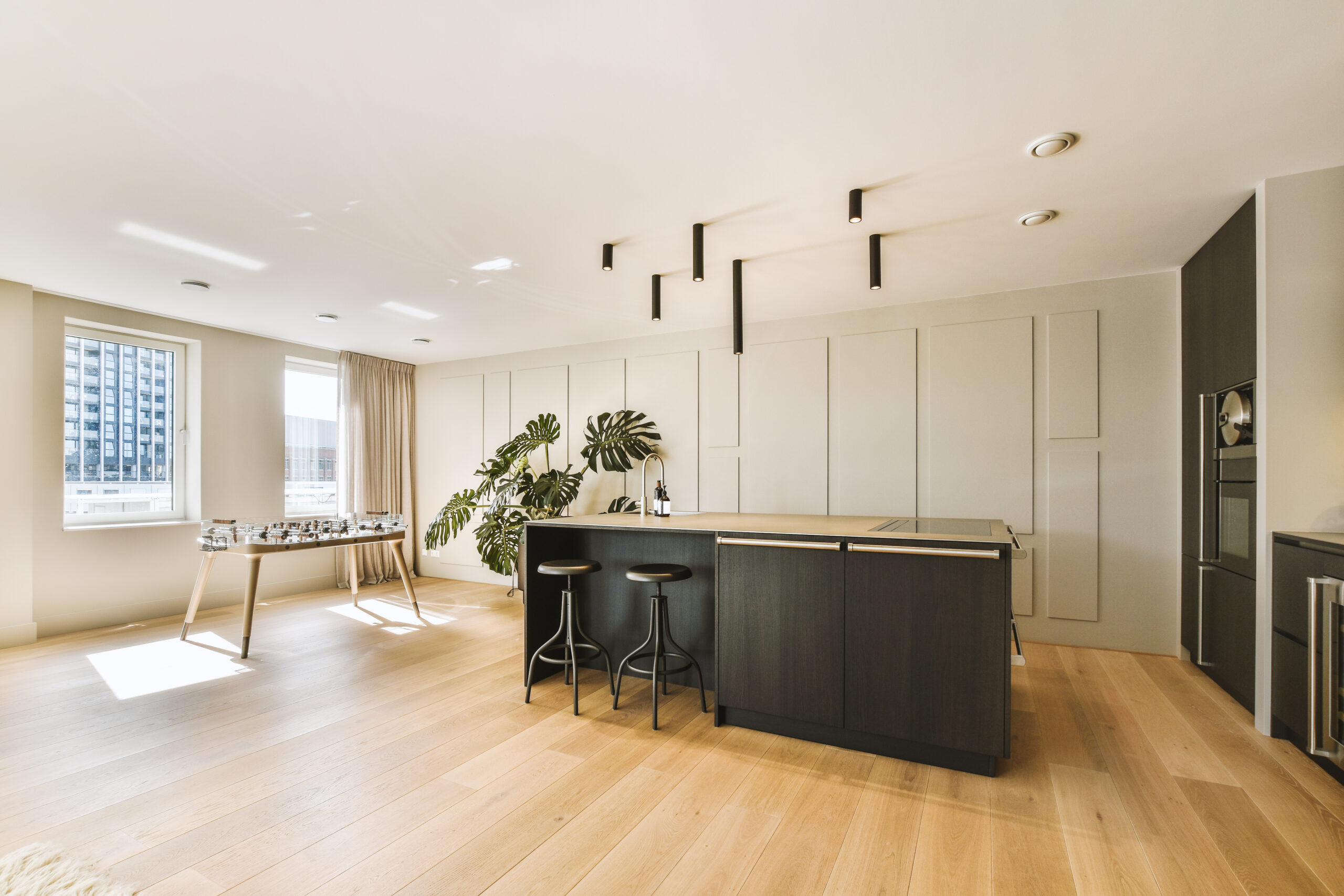 Contemporary minimalist style interior design of light studio apartment with wooden table and chairs in dining zone between open kitchen and living room with white walls and parquet floor