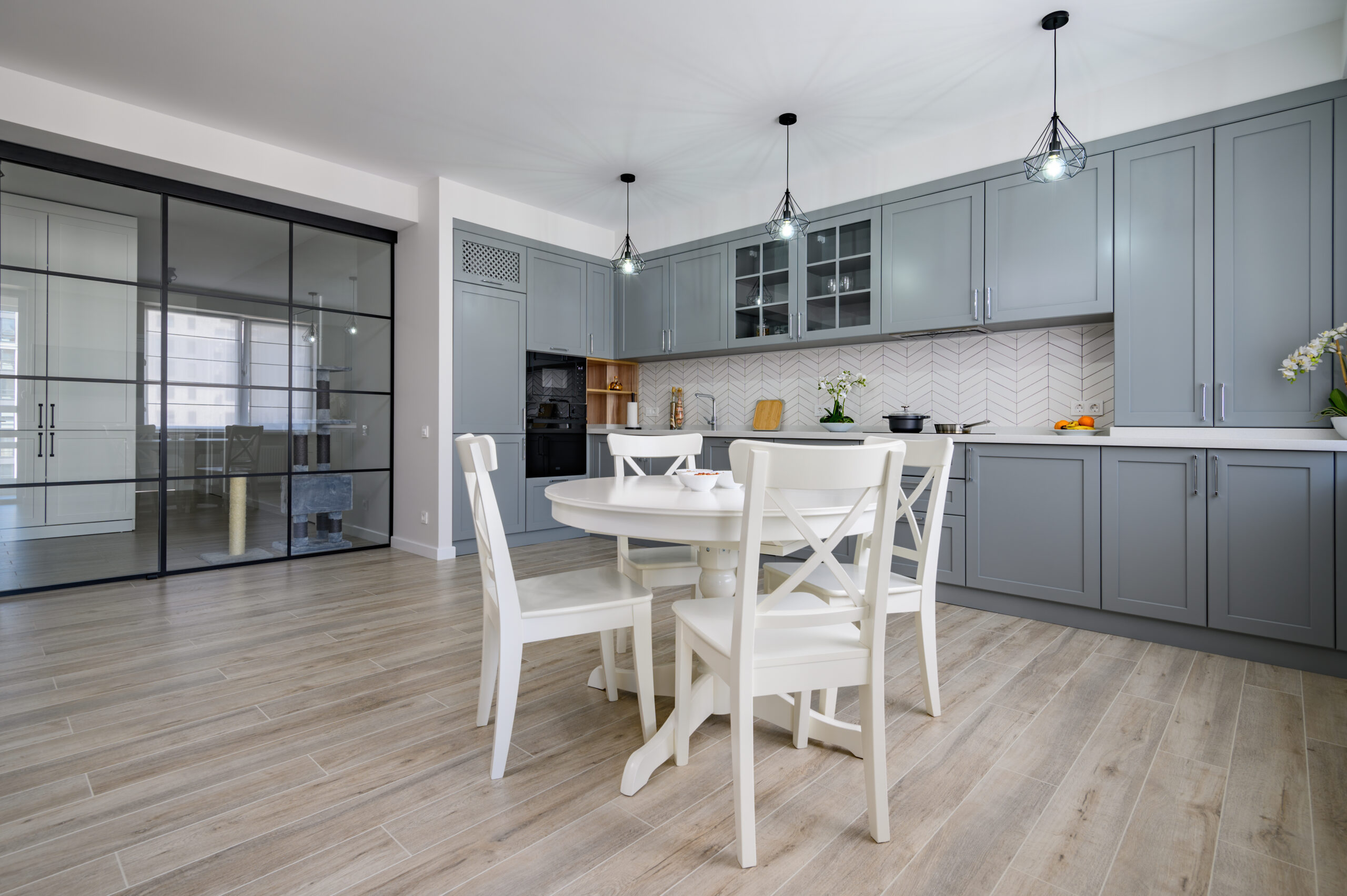 Trendy grey and white modern kitchen with white round dining table in studio apartment