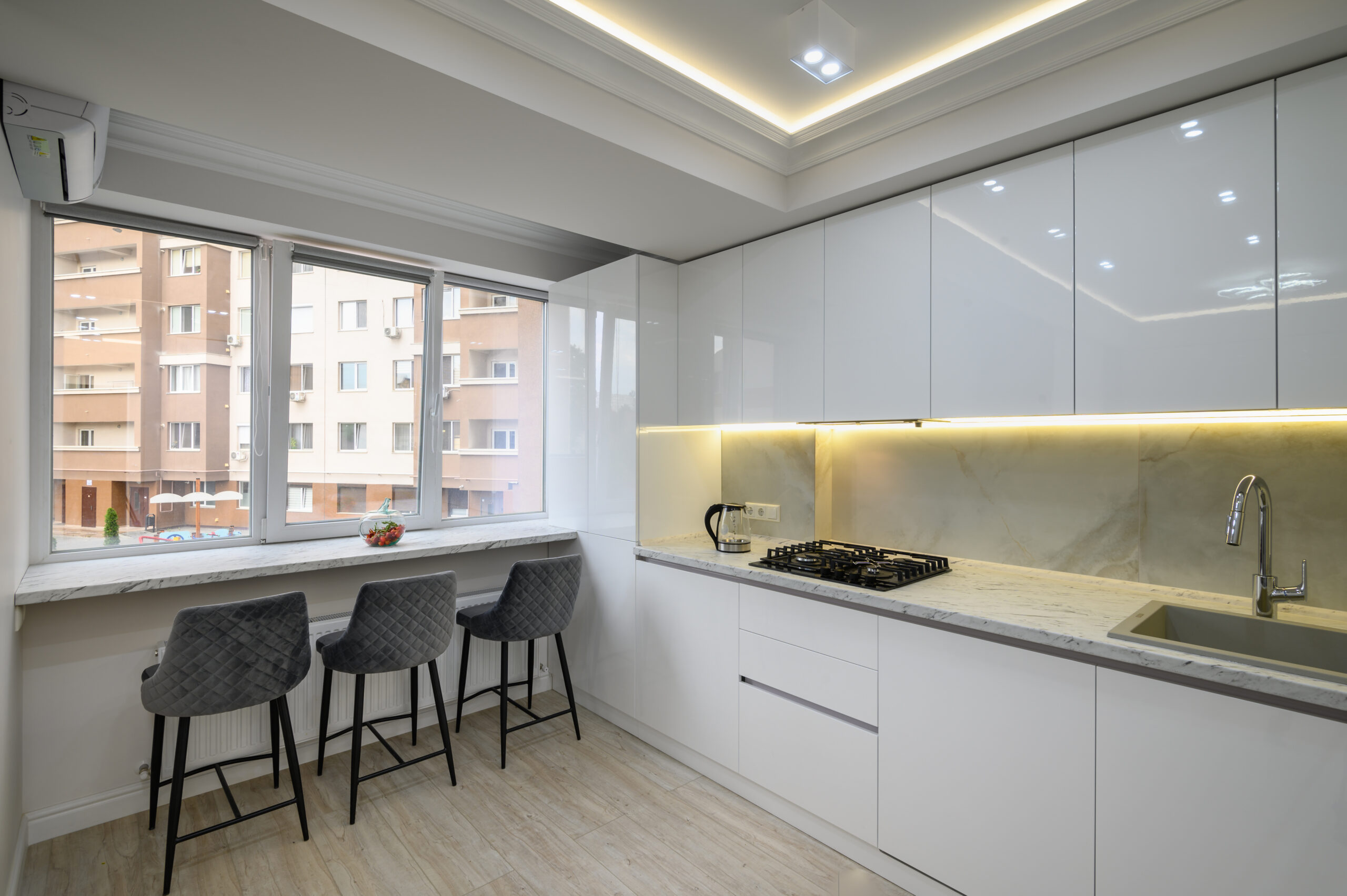 Kitchen with a stove top, dining chairs next to a window, city view outside of window