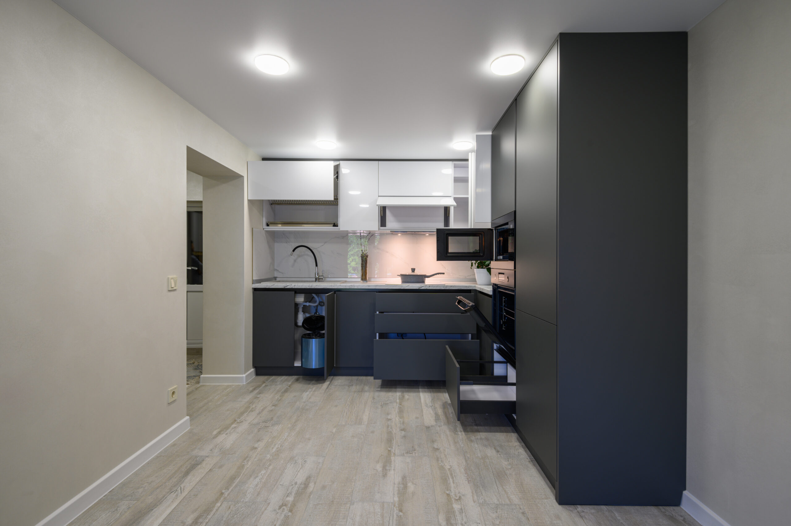Showcase interior of modern simple dark grey and white kitchen, drawers retracted, doors open