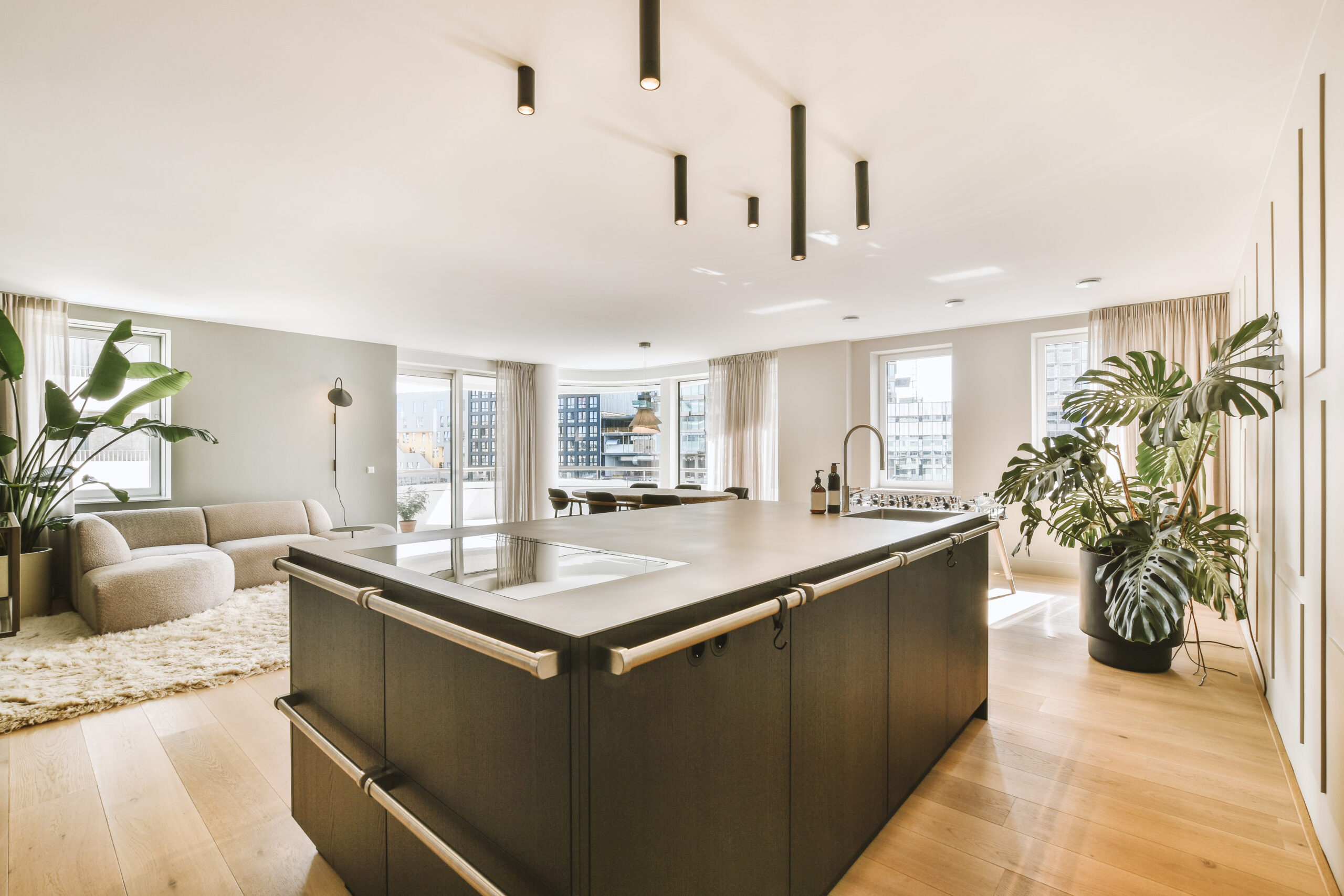 Contemporary minimalist style interior design of light studio apartment with wooden table and chairs in dining zone between open kitchen and living room with white walls and parquet floor