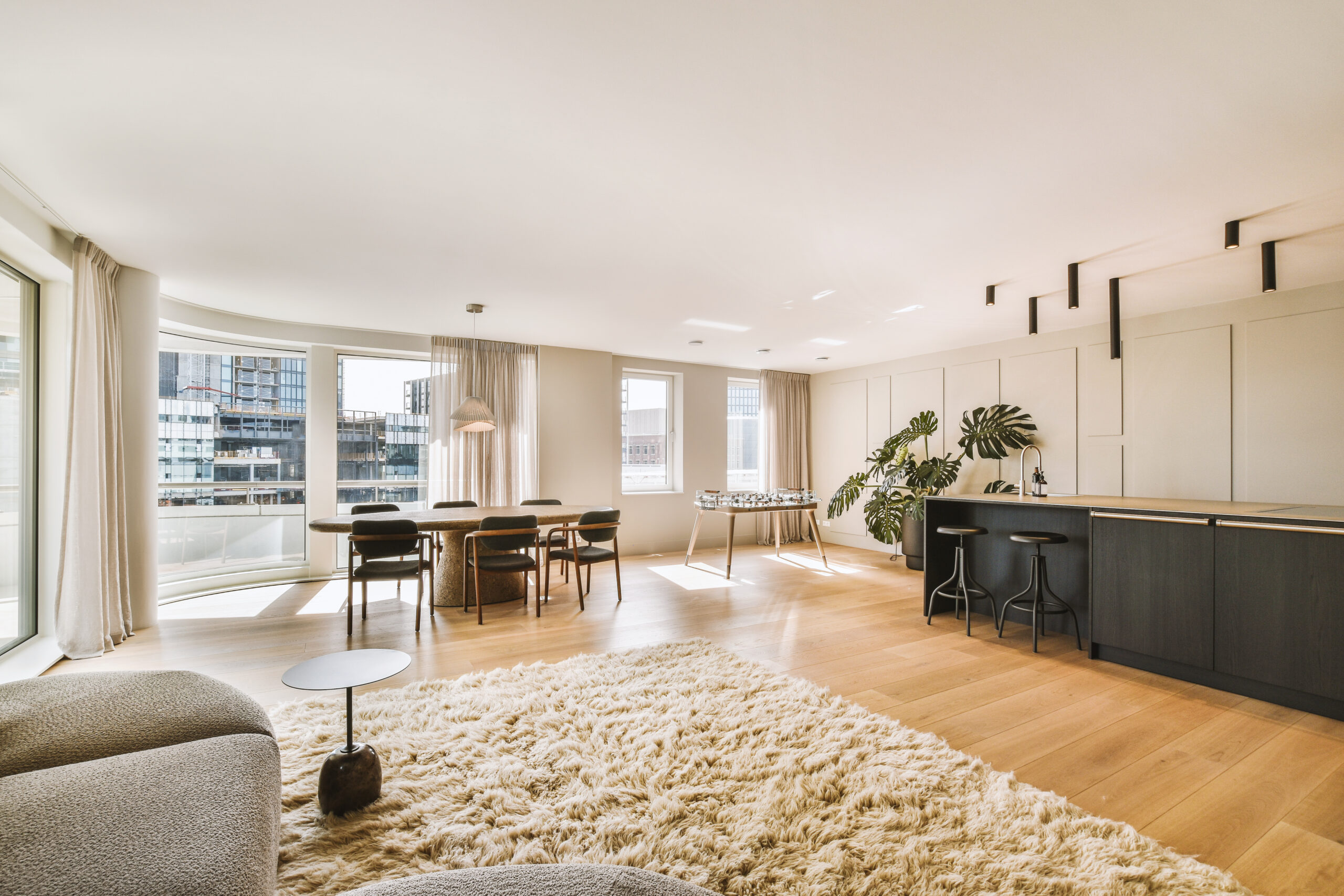 Contemporary minimalist style interior design of light studio apartment with wooden table and chairs in dining zone between open kitchen and living room with white walls and parquet floor