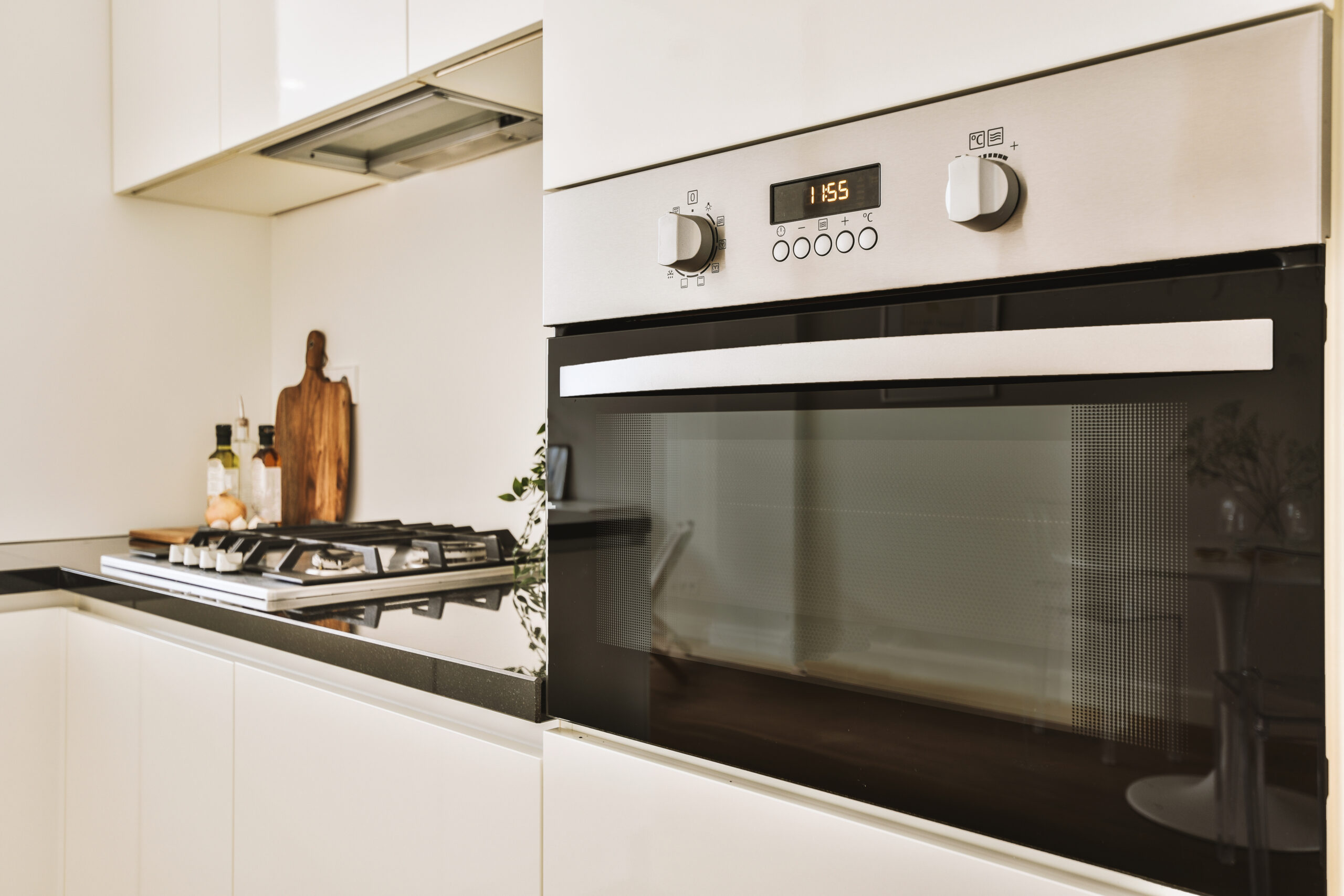 Fragment of interior of light narrow home kitchen with minimalist style white furniture with sink and stove