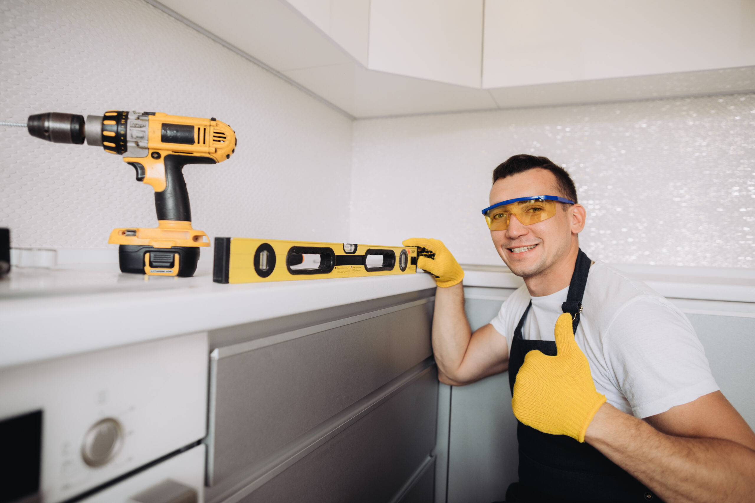 Maintenance man installing kitchen furniture in a black apron and yellow gloves using a level measurement tool