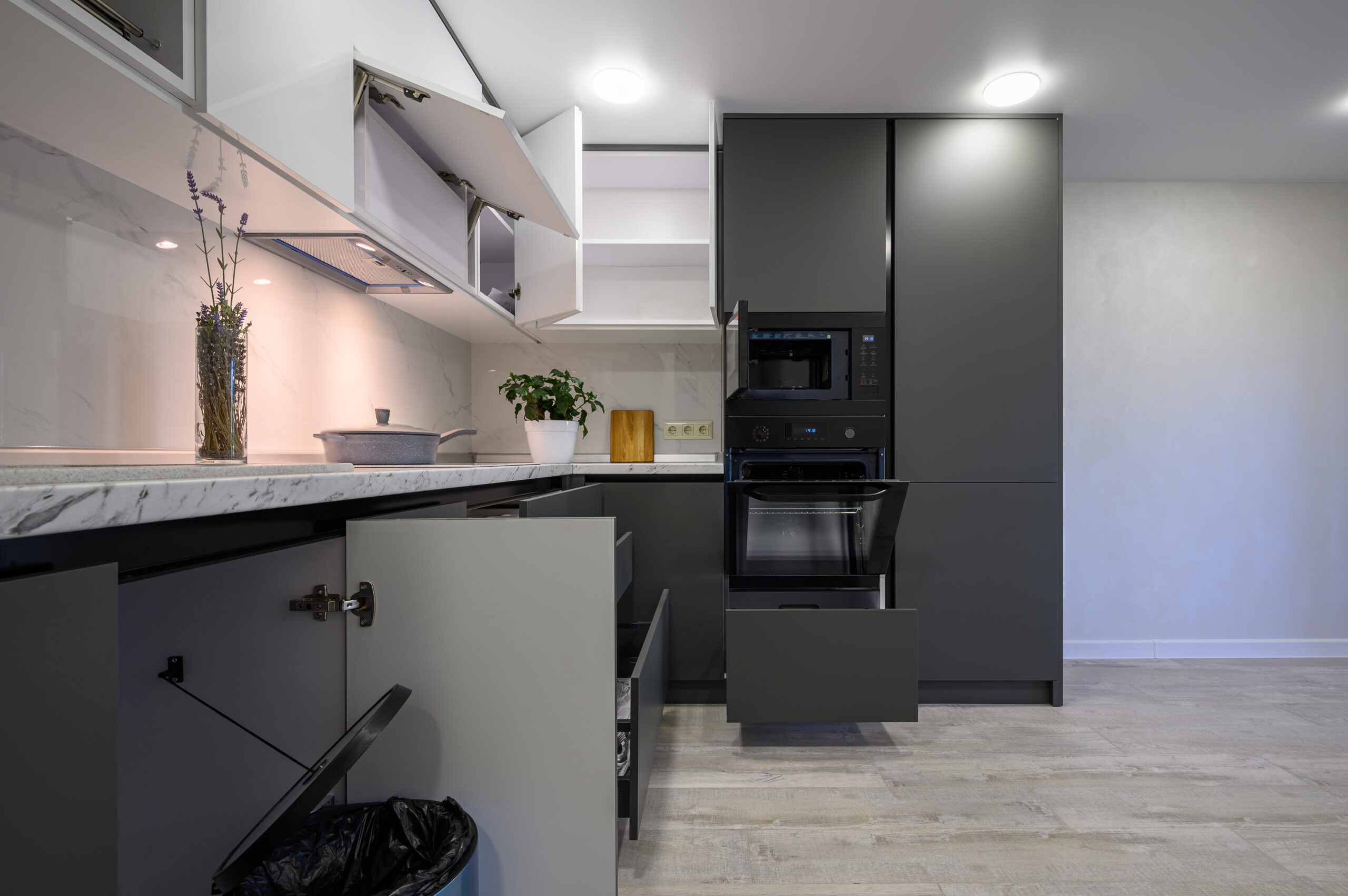 Showcase interior of modern simple dark grey and white kitchen, drawers retracted, doors open