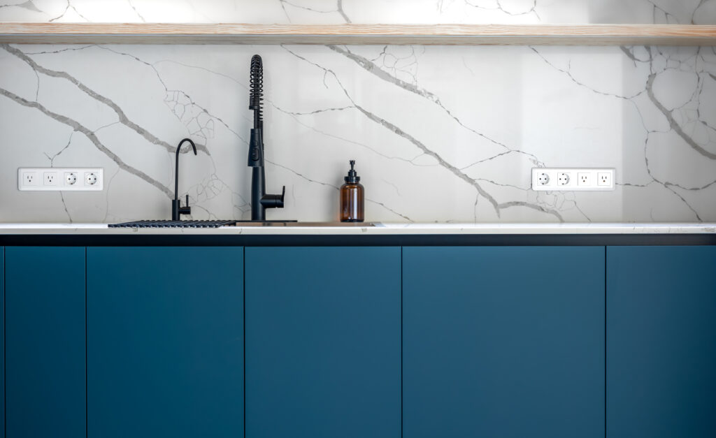 A close-up view of a sleek kitchen with a black faucet, white marble wall with gray veins, and deep blue minimalist cabinetry. Elegant and clean aesthetic.