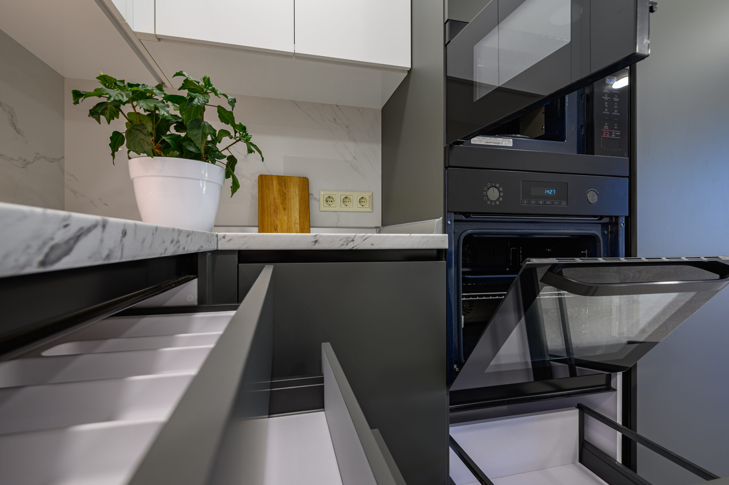 Closeup to marble worktop of modern dark grey and white kitchen, cooking pan at gas cooker, cabinet drawers retracted, oven door open